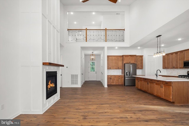 kitchen featuring dark wood-type flooring, a high ceiling, hanging light fixtures, tasteful backsplash, and stainless steel appliances