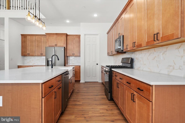 kitchen featuring stainless steel appliances, tasteful backsplash, light hardwood / wood-style flooring, decorative light fixtures, and a kitchen island with sink