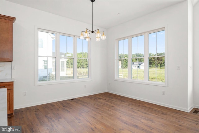 unfurnished dining area with dark hardwood / wood-style flooring, plenty of natural light, and a notable chandelier