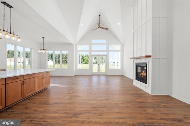 unfurnished living room featuring ceiling fan with notable chandelier, high vaulted ceiling, a wealth of natural light, and dark wood-type flooring