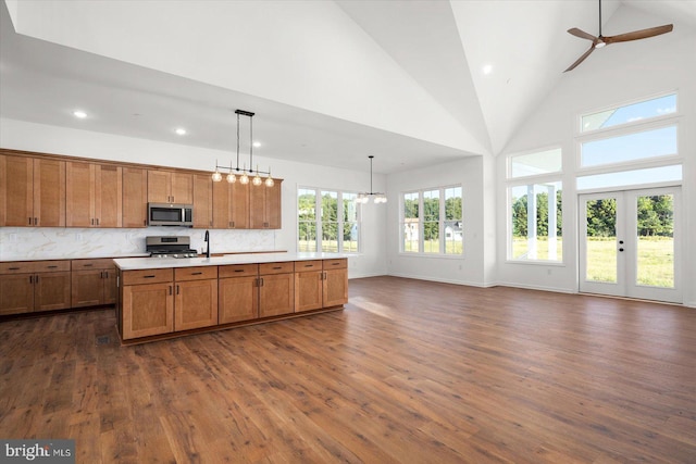 kitchen with high vaulted ceiling, hanging light fixtures, appliances with stainless steel finishes, a healthy amount of sunlight, and dark hardwood / wood-style flooring