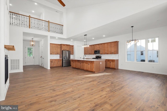 kitchen with pendant lighting, a healthy amount of sunlight, a kitchen island with sink, and appliances with stainless steel finishes