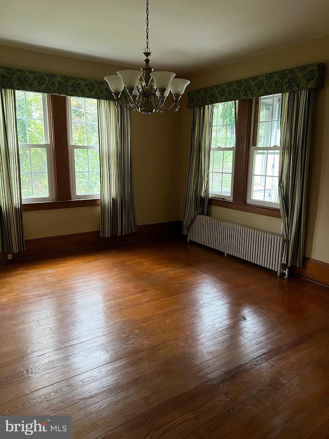 unfurnished room with wood-type flooring, radiator heating unit, and a notable chandelier