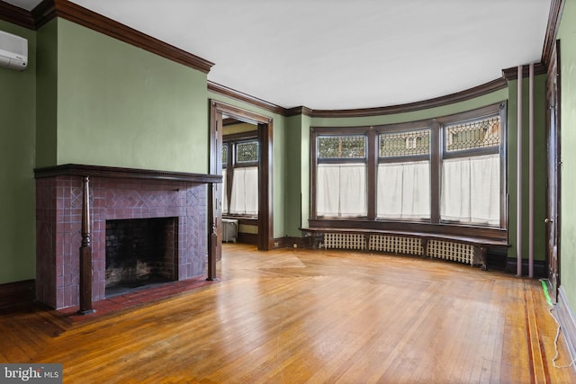 unfurnished living room featuring a tiled fireplace, radiator heating unit, light wood-type flooring, crown molding, and a wall mounted AC