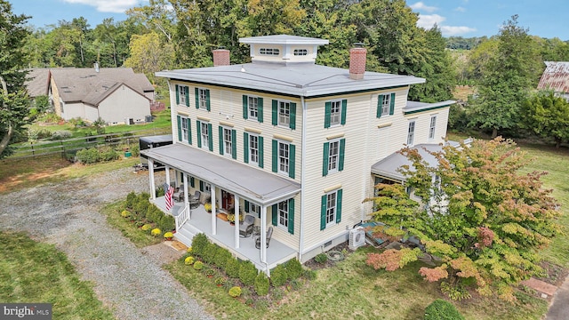 view of front of house with covered porch, gravel driveway, and a chimney
