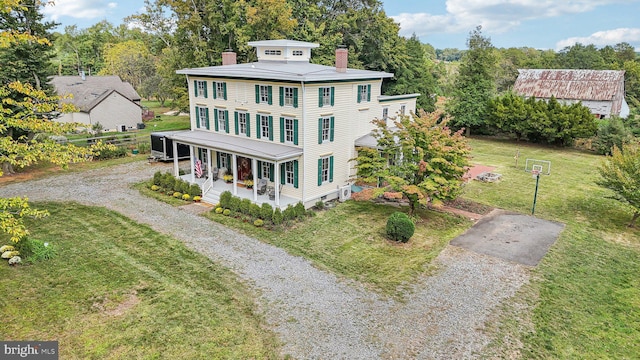 view of front of home featuring a chimney, a porch, a front lawn, and gravel driveway
