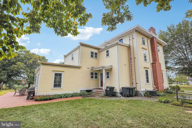 rear view of property with a chimney, a patio area, central AC, a yard, and fence