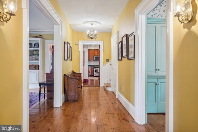hall featuring a chandelier, hardwood / wood-style flooring, and baseboards
