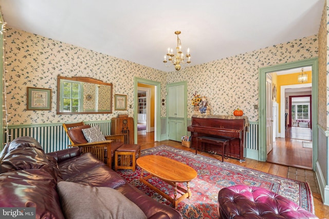 living room featuring a chandelier, wallpapered walls, wood finished floors, and baseboards
