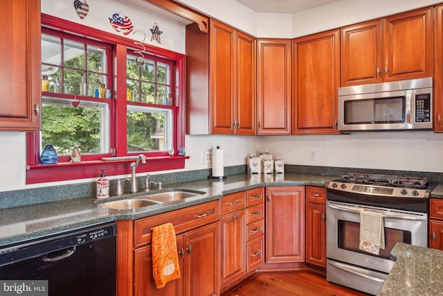 kitchen with a sink, dark wood-style floors, brown cabinetry, dark stone counters, and stainless steel appliances