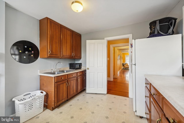 kitchen featuring black microwave, light countertops, freestanding refrigerator, brown cabinetry, and a sink