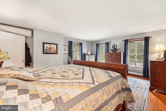 bedroom with baseboard heating, hardwood / wood-style flooring, and a wall mounted air conditioner