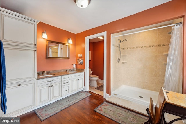 full bathroom featuring a sink, a tile shower, wood finished floors, and toilet