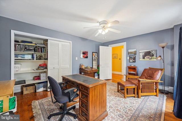 office space featuring wood finished floors, a baseboard heating unit, and a ceiling fan