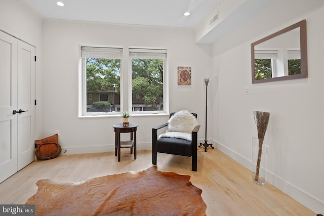 living area with a healthy amount of sunlight, crown molding, and light hardwood / wood-style flooring