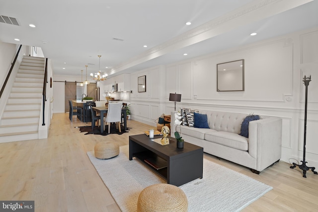 living room featuring light wood-type flooring, crown molding, a barn door, and a notable chandelier