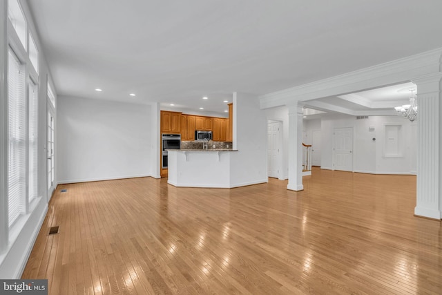 unfurnished living room with light wood-type flooring, crown molding, and an inviting chandelier