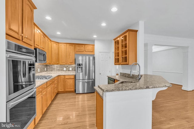 kitchen featuring light hardwood / wood-style floors, light stone counters, kitchen peninsula, stainless steel appliances, and sink