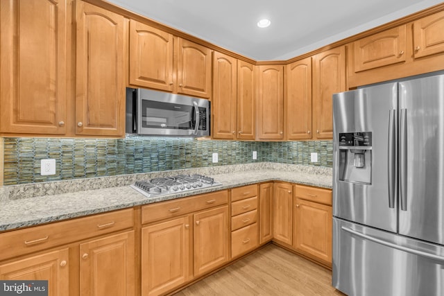 kitchen with light stone countertops, stainless steel appliances, light hardwood / wood-style floors, and tasteful backsplash