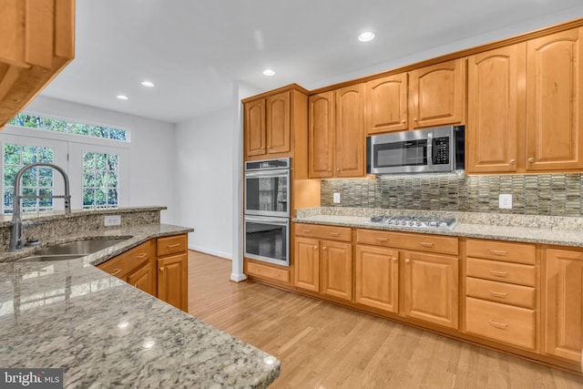 kitchen with appliances with stainless steel finishes, light wood-type flooring, sink, and light stone counters