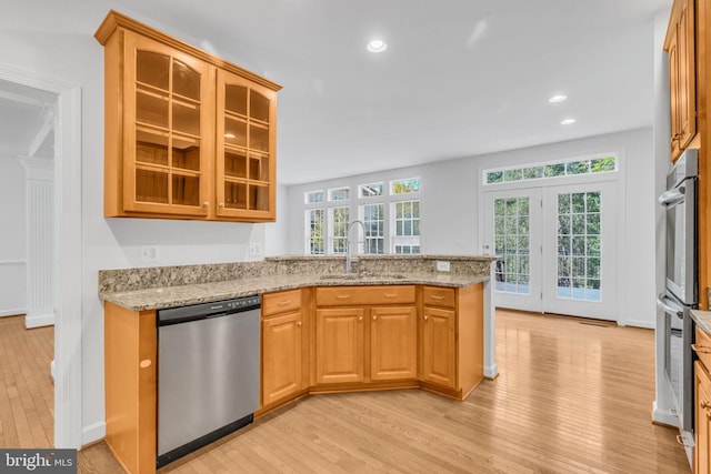 kitchen with light stone counters, sink, stainless steel appliances, and light hardwood / wood-style floors