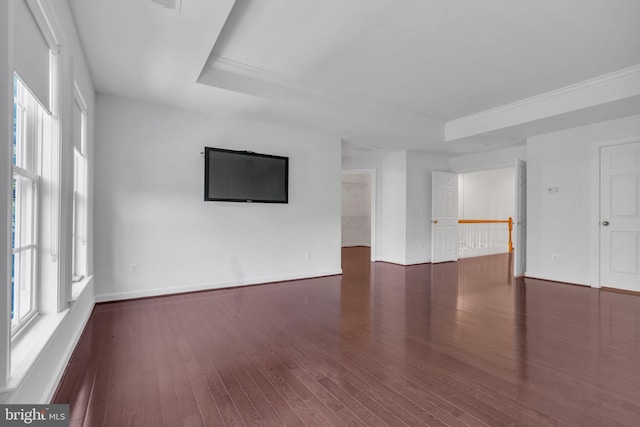 empty room featuring a raised ceiling, dark hardwood / wood-style floors, and crown molding