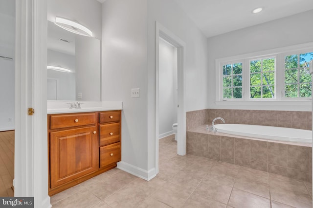 bathroom with vanity, a relaxing tiled tub, toilet, and tile patterned floors