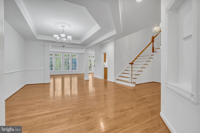 unfurnished living room featuring a raised ceiling, light hardwood / wood-style flooring, decorative columns, ornamental molding, and a notable chandelier