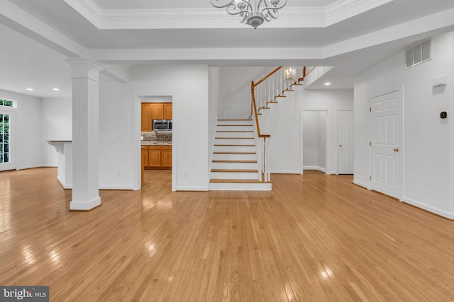 unfurnished living room featuring decorative columns, crown molding, light hardwood / wood-style floors, and a chandelier