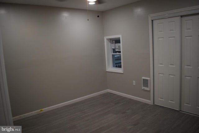 unfurnished bedroom with heating unit, a closet, and dark hardwood / wood-style floors