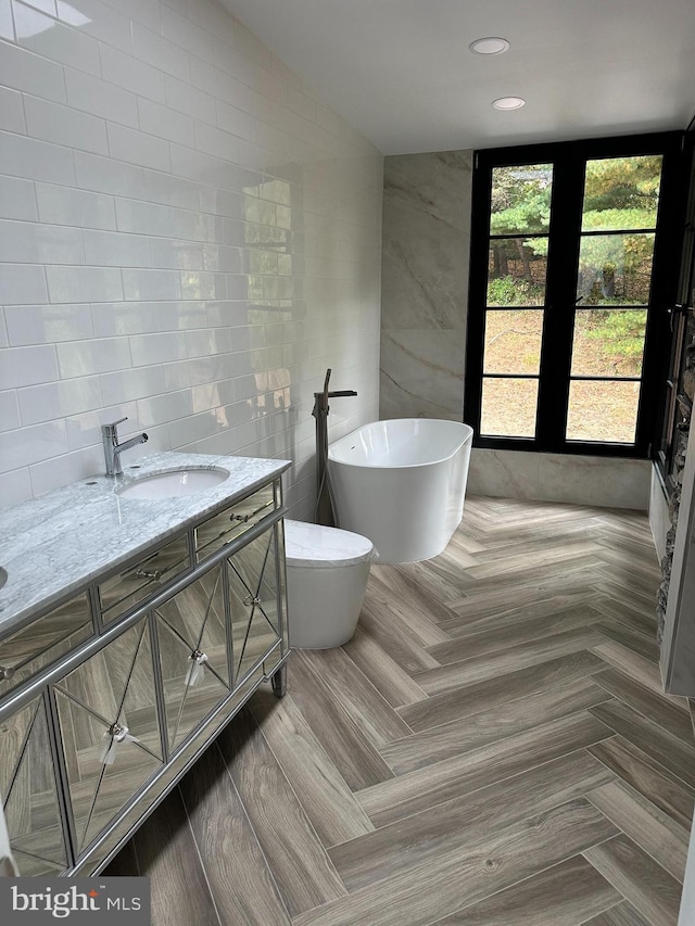 bathroom with vanity, a washtub, and tile walls