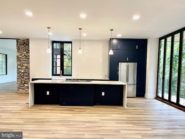 kitchen featuring a spacious island, floor to ceiling windows, hanging light fixtures, light hardwood / wood-style flooring, and stainless steel refrigerator