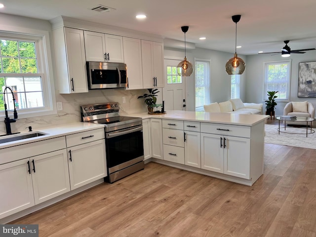 kitchen featuring a peninsula, a sink, visible vents, open floor plan, and appliances with stainless steel finishes