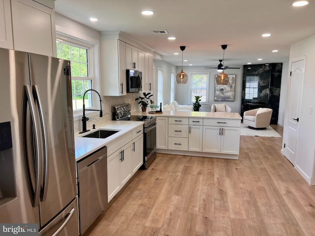 kitchen with light wood finished floors, stainless steel appliances, visible vents, a sink, and a peninsula