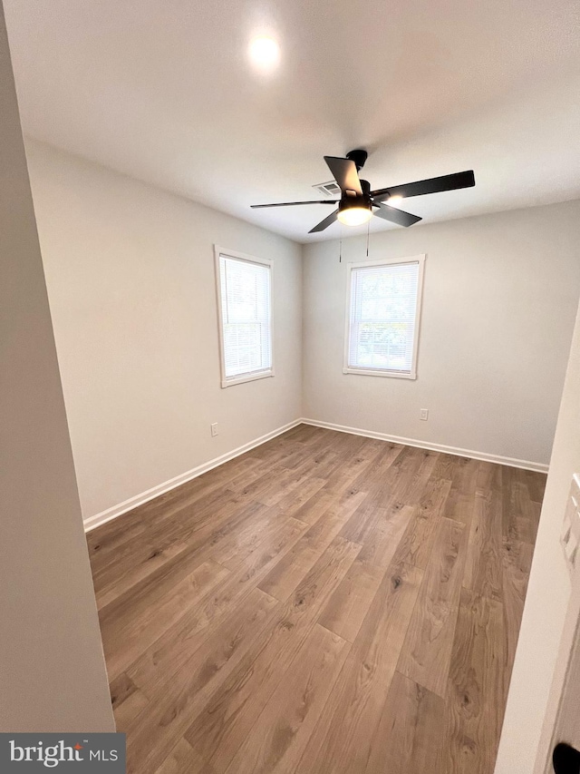 empty room with wood finished floors, a ceiling fan, and baseboards