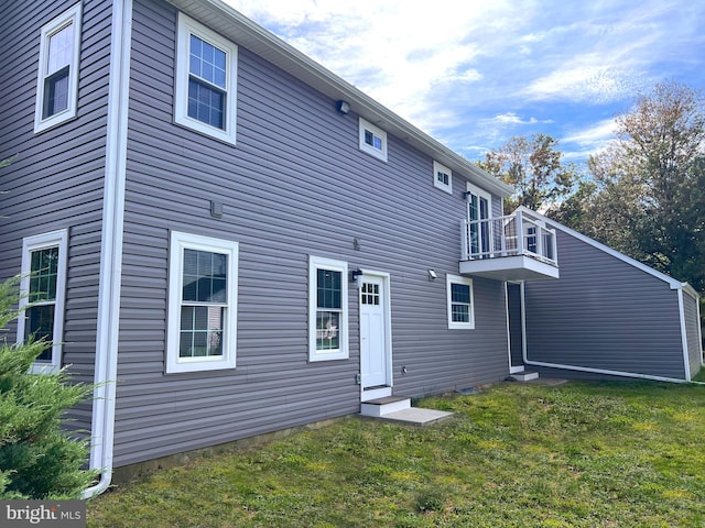 back of property with entry steps, a lawn, and a balcony