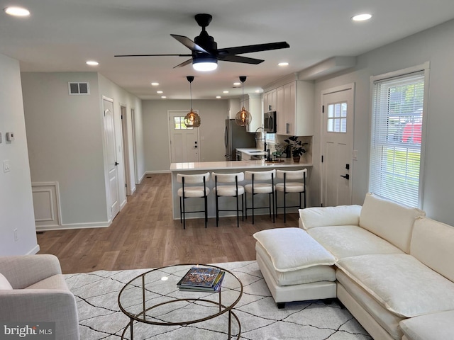 living area with recessed lighting, visible vents, a ceiling fan, light wood-type flooring, and baseboards