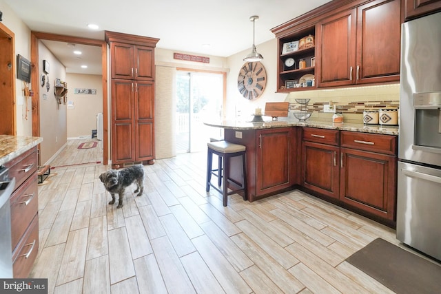 kitchen with a breakfast bar area, light hardwood / wood-style flooring, decorative light fixtures, light stone countertops, and stainless steel refrigerator with ice dispenser