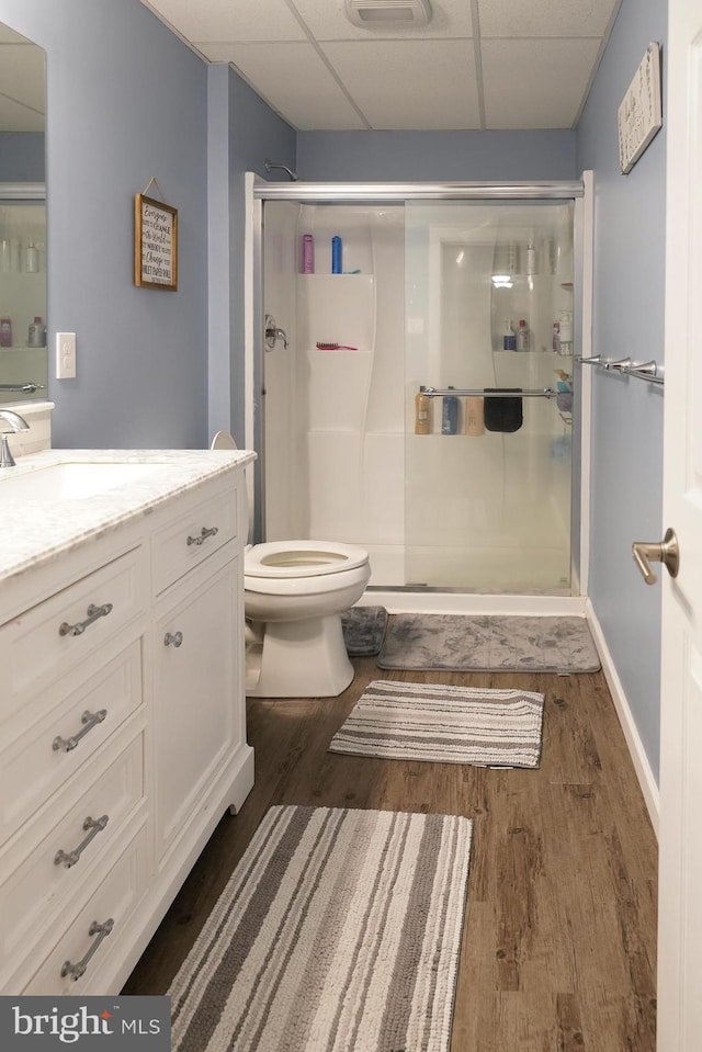 bathroom featuring toilet, a paneled ceiling, a shower with shower door, hardwood / wood-style flooring, and vanity