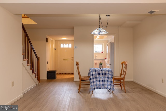 dining area featuring light wood-type flooring, visible vents, baseboards, and stairs