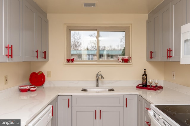 kitchen with white appliances, a sink, visible vents, and light stone countertops