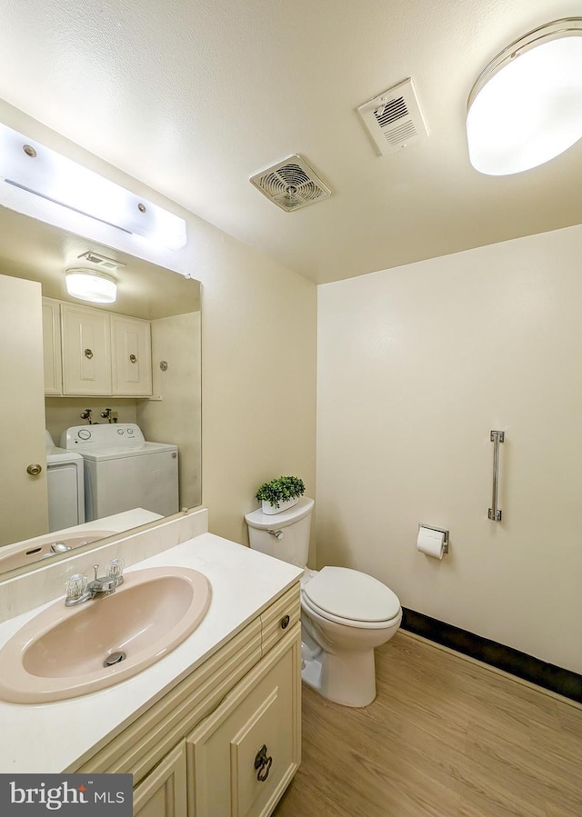 bathroom featuring washing machine and dryer, visible vents, toilet, and wood finished floors