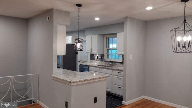 kitchen featuring light stone countertops, refrigerator, sink, white cabinetry, and hanging light fixtures