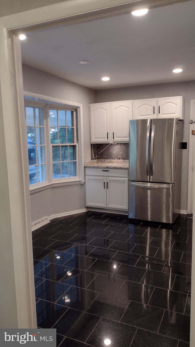 kitchen with backsplash, stainless steel refrigerator, and white cabinets