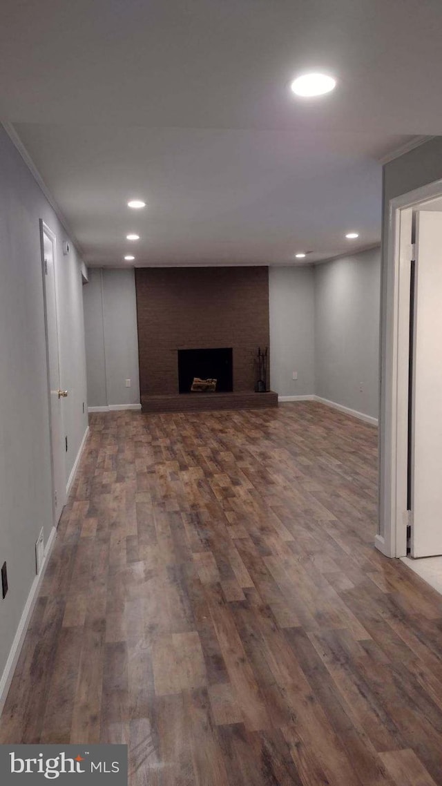 basement featuring ornamental molding, a brick fireplace, and dark wood-type flooring