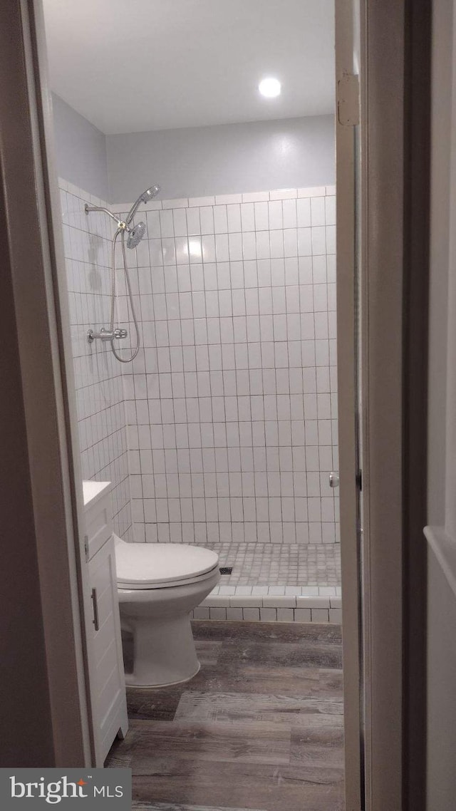 bathroom with hardwood / wood-style floors, vanity, a tile shower, and toilet