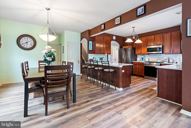 kitchen featuring light hardwood / wood-style floors, a breakfast bar area, hanging light fixtures, decorative backsplash, and stainless steel appliances