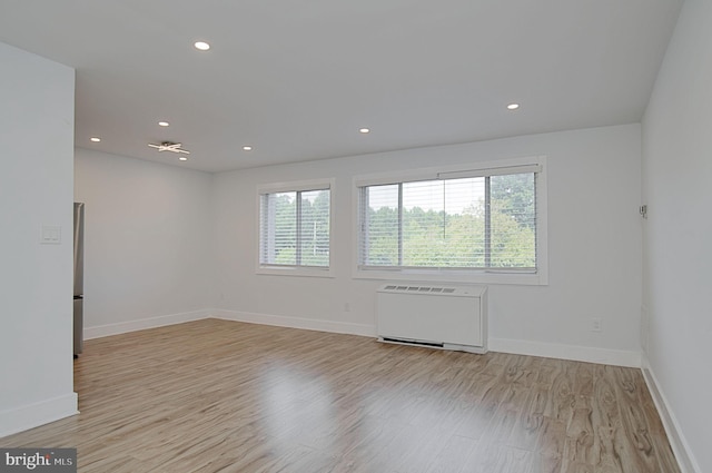 empty room with light hardwood / wood-style flooring, plenty of natural light, and radiator heating unit