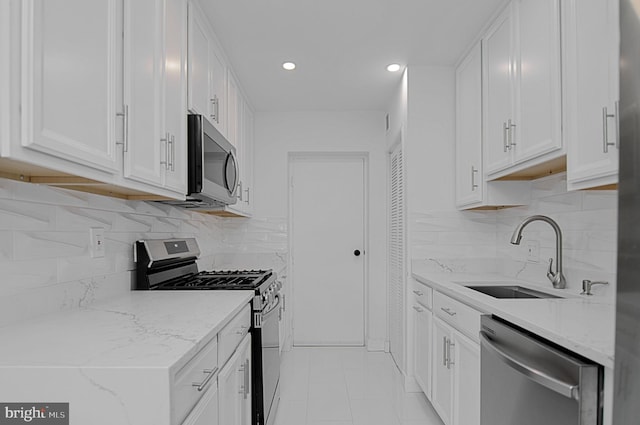 kitchen featuring sink, white cabinetry, stainless steel appliances, backsplash, and light stone countertops