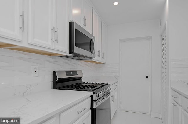 kitchen with white cabinetry, stainless steel appliances, backsplash, light tile patterned floors, and light stone countertops